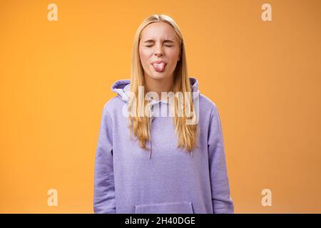 Spielerisch amüsiert charismatische junge lustige blonde Mädchen mit Spaß enge Augen zeigt Zunge rebellischen Narr um störte enjoyin Stockfoto