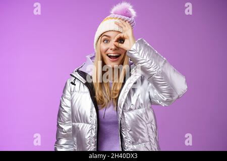 Beeindruckt neugierig gut aussehende blonde stilvolle weibliche Reisende bezaubert verschneiten Bergblick halten okay ok Zeichen Auge lächelnd erstaunlich Stockfoto