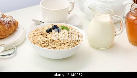 Rohe Haferflocken in weißer Keramikplatte auf weißem Tisch, Frühstück, Nahaufnahme Stockfoto
