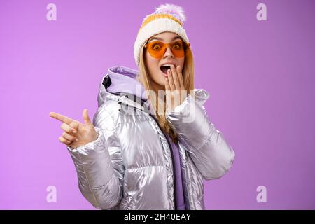Erstaunt sprachlos überrascht attraktive stilvolle blonde Freundin in Sonnenbrille, silber glitzernde Jacke Hut Drop Kiefer beeindruckt w Stockfoto