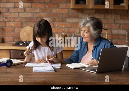 Ältere Großmutter hilft der Enkelin, Hausaufgaben zu machen Stockfoto