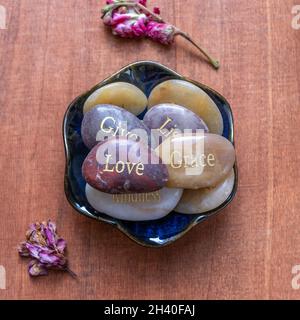 Motivierende inspirierende Steine mit Schriften. Gelassenheit, Dankbarkeit, Leidenschaft, Liebe auf rotem Tischhintergrund Stockfoto