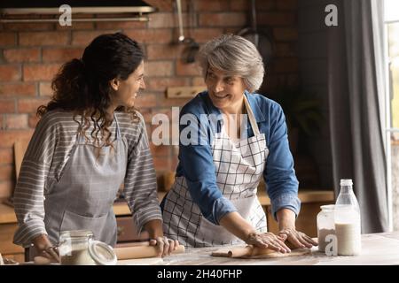 Glückliche, lateinamerikanische Tochter und ältere Mutter, die zu Hause kocht Stockfoto