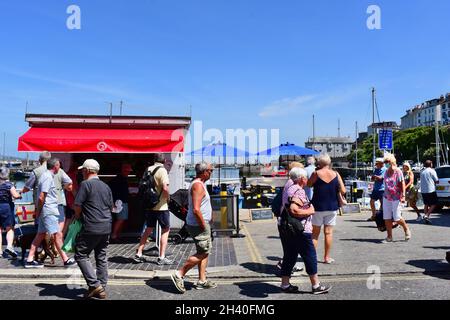 Urlauber schlendern gerne am Rande des Hafens in Brixham entlang. Stände und Open-Air-Cafés. Stockfoto