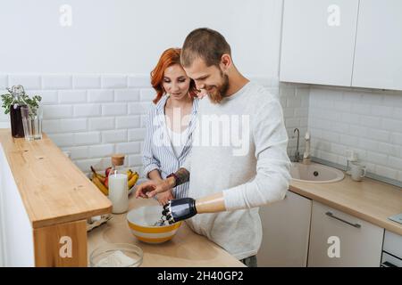 Schönes dreißigjähriges Paar, das in der Küche zusammen kochte und Eier hastete. Die Frau beobachtet den enthusiastischen Ehemann, unterstützt ihn und sorgt sich. Er hat es Stockfoto