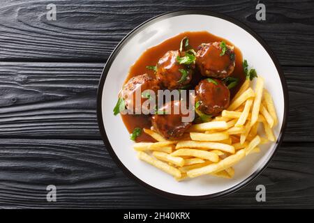 Boulets liegeois Liege Fleischbällchen in Apfelsauce und Pommes Frites in der Nähe auf dem Teller auf dem Tisch. Horizontale Draufsicht von oben Stockfoto