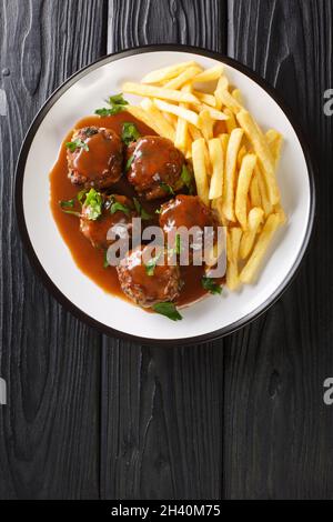 Boulets liegeois ist ein beliebtes Gericht, das in ganz Belgien aus Fleischbällchen serviert wird, die in einer Apfel- und Zwiebelsoße schwimmen und in der pla mit Pommes in der Nähe serviert werden Stockfoto