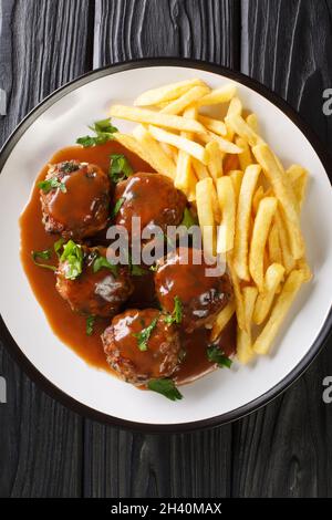 Boulet a la liegeoise oder boulet Sauce Lapin ist ein belgisches Gericht aus Fleischbällchen in Apfelsauce und Pommes frites in der Nähe auf dem Teller auf dem Tisch. Vertikal Stockfoto