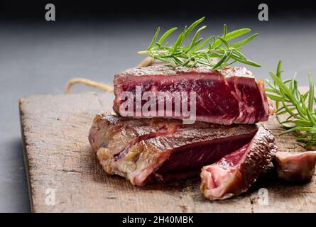 Gebratenes Stück Rinderribeye, auf einem braunen Holzbrett in Stücke geschnitten, seltener Doneness Stockfoto