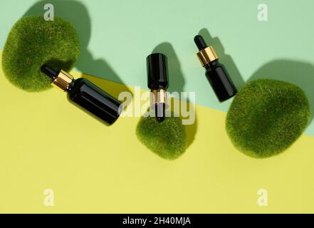 Braune Glasflaschen mit einer Pipette auf grün-gelbem Hintergrund und Moosstücken. Kosmetik SPA Branding Mockup, top Stockfoto