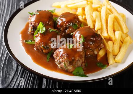 Boulets liegeois Liege Fleischbällchen in Apfelsauce und Pommes Frites in der Nähe auf dem Teller auf dem Tisch. Horizontal Stockfoto