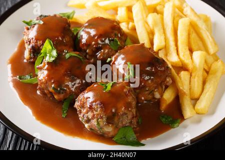 Boulets a la Liegeoise ein klassischer belgischer Fleischball in Apfelsauce und Pommes Frites in der Nähe auf dem Teller auf dem Tisch. Horizontal Stockfoto