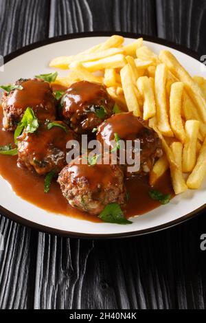 Boulet a la liegeoise oder boulet Sauce Lapin ist ein belgisches Gericht aus Fleischbällchen in Apfelsauce und Pommes frites in der Nähe auf dem Teller auf dem Tisch. Vertikal Stockfoto