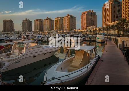 Porto Arabia Marina in der Perle Doha, Katar Sonnenuntergang Aufnahme zeigt luxuriöse Yachten angedockt an der Marina mit Wohngebäuden im Hintergrund. Stockfoto