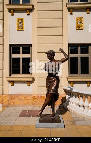 SKOPJE, NORDMAKEDONIEN - 19. AUGUST 2021: Bronzeskulptur einer tanzenden Frau vor einem Gebäude bei Sonnenuntergang Stockfoto