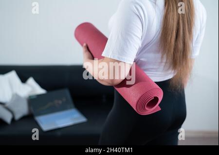 Junge mollige Frau faltet Sportmatte nach dem Online-Fitnesskurs Stockfoto