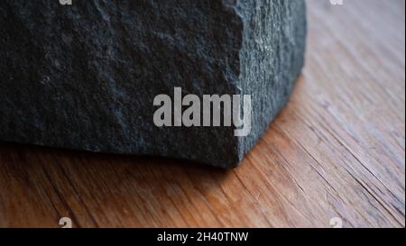 Handgeschnittener Granitblock auf einer rustikalen Holzoberfläche; geringe Schärfentiefe mit Fokus auf raue Kanten. Stockfoto