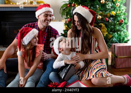 Glückliche kaukasische Familie trägt weihnachtsmütze und packt Geschenke zur weihnachtszeit aus Stockfoto