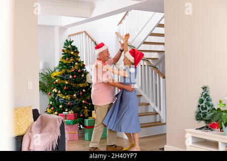 Glückliches kaukasisches Seniorenpaar mit Weihnachtsmütze, das zur weihnachtszeit tanzt Stockfoto