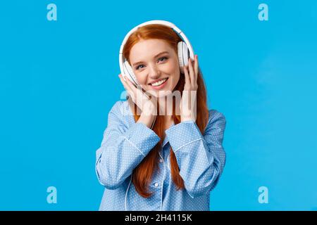 Technologie, Lifestyle und People Concept. Süße Rothaarige Frau im Pyjama, hören Sie Musik in Kopfhörern, genießen Sie schöne Beats im Kopfhörer Stockfoto