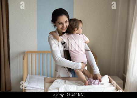 Lächelnd, fürsorgliche junge Mutter, die ihre Babykleidung wechselt, Windel auf dem Tisch Stockfoto