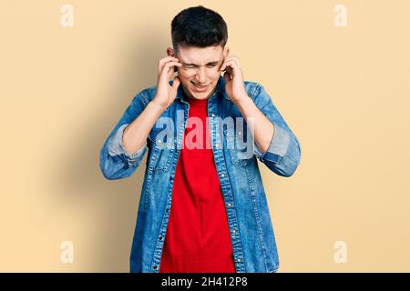 Junge kaukasische Junge mit Ohren Erweiterung tragen lässige Denim-Jacke bedeckt Ohren mit Fingern mit verärgerten Ausdruck für den Lärm der lauten Musik. dea Stockfoto