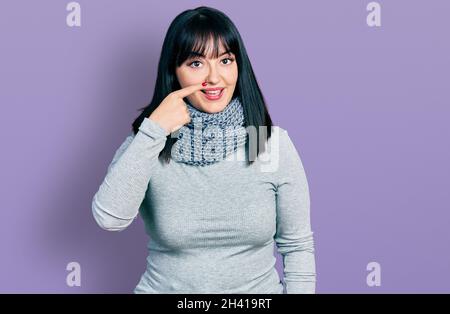Junge hispanische plus size Frau trägt Winter Schal zeigt mit Hand Finger zu Gesicht und Nase, lächelnd fröhlich. Beauty-Konzept Stockfoto