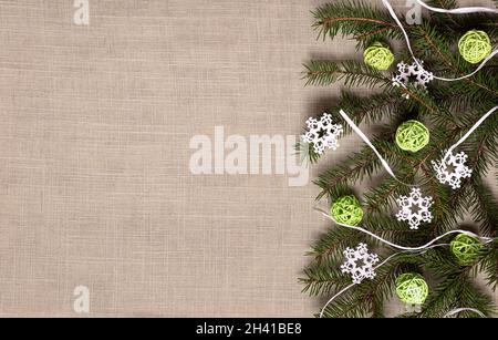 Tannenzweig mit grünen Rattankugeln, weißen Schneeflocken aus Holz und Bast auf beigefarbenem Leinenmaterial. Flache Laie mit natürlich recycelbaren Dekorelementen. Stockfoto