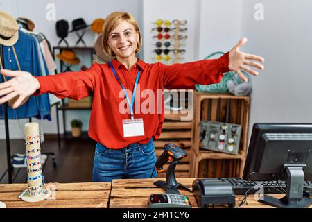 Eine blonde Frau mittleren Alters, die als Managerin in einer Einzelhandelsboutique arbeitet und die Kamera lächelt, um sich zu umarmen. Fröhlicher Ausdruck embrac Stockfoto