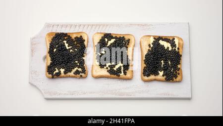 Paddelfischkaviar auf einer quadratischen Scheibe Weizenmehl-Brot auf einem hölzernen Schneidebrett. Draufsicht auf weißem Tisch Stockfoto