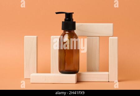 Braune Glasflasche mit schwarzer Pumpe von Kosmetikprodukten auf Holzblock auf orangefarbenem Papierhintergrund. Natürliche Bio-Spa-Kosmetik Stockfoto