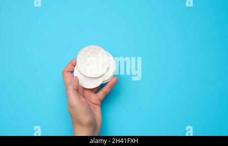 Weibliche Hand hält saubere runde weiße Baumwolle Make-up-Entferner Pads auf blauem Hintergrund Stockfoto