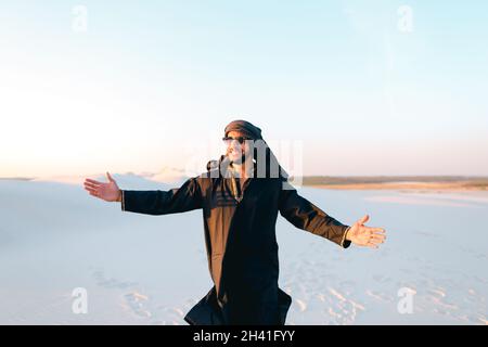 Fröhlicher Araber, wandert durch die Wüste, lächelt und genießt das Leben am Sommerabend. Stockfoto