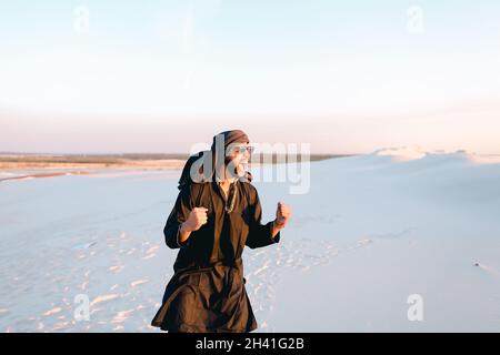 Fröhlicher Araber, wandert durch die Wüste, lächelt und genießt das Leben am Sommerabend. Stockfoto