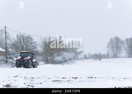 Woodbridge Suffolk UK Februar 07 2021: Ein roter Traktor parkte am Rande eines Farmfeldes in einem schweren Schneesturm auf dem britischen Land Stockfoto