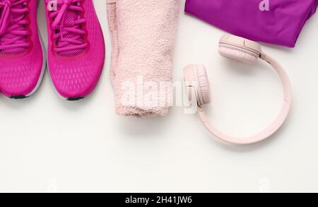 Ein Paar lila Textil-Sportschuhe, kabellose Kopfhörer, ein Handtuch und eine Flasche Wasser auf weißem Hintergrund. Sportbekleidung Stockfoto