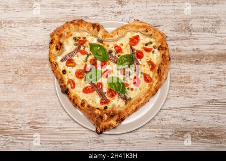 Herzförmige Pizza mit Sardellen aus der Dose, Basilikumblättern, Kirschtomaten und Mozzarella-Käse Stockfoto
