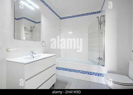 Badezimmer mit verglaster Badewanne und weißem Schminktisch und blauem Blumenrand in der Ferienwohnung Stockfoto