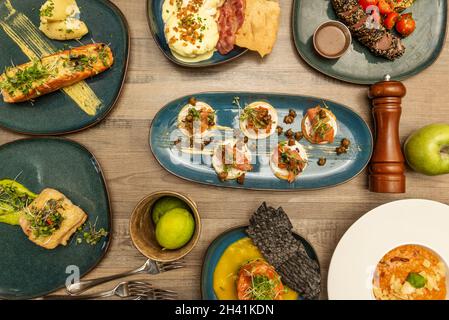 Set von internationalen Gerichten mit Fisch, gegrilltem Lachs, norwegischem Lachs Blinis, rotem Thunfisch Tataki, Seehecht in Sauce, Tartare, Limetten, Gabeln und Pfeffer Stockfoto