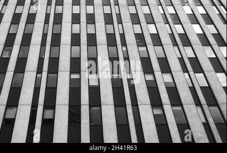 Nahaufnahme eines Bürogebäudes im brutalistischen Hochhausstil mit weißen vertikalen Betonlinien und dunklen Fenstern Stockfoto