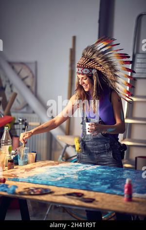 Eine junge Künstlerin mit Kriegshaube arbeitet gerne in angenehmer Atmosphäre im Atelier an ihrem neuen Gemälde. Kunst, Malerei, Atelier Stockfoto