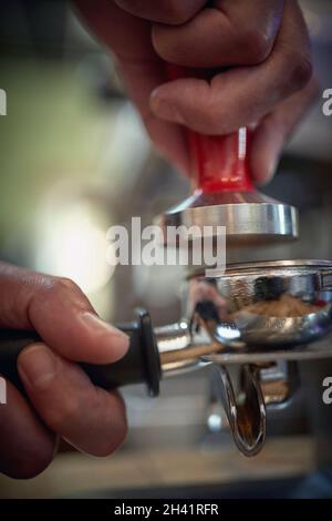 Nahaufnahme der Hände des Barkeepers, der duftenden und aromatischen gemahlenen Kaffee für einen Espresso presst. Kaffee, Getränke, Bar Stockfoto