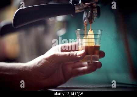 Ein Barkeeper hält ein kleines Glas in der Hand und füllt es mit einem aromatischen und duftenden Getränk in einem Espresso-Apparat. Kaffee, Getränke, Bar Stockfoto