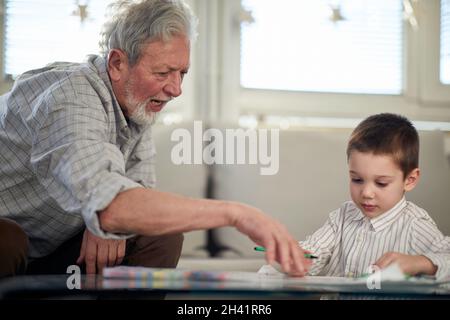 Ein Opa lehrt seinem Enkel, wie man zeichnet, während er eine Zeit in entspannter Atmosphäre zu Hause zusammen verbringt. Familie, Zuhause, Freizeit Stockfoto