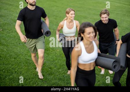 Menschen wandern mit Fitnessmatten auf grüner Wiese Stockfoto