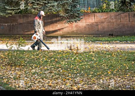 Dnepropetrovsk, Ukraine - 10.19.2021: Reinigung trockener Blätter mit einer Windmühle. Ein kommunaler Arbeiter säubert den Stadtpark. Stadtparks für den Winter vorbereiten Stockfoto