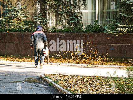 Trockene Blätter mit einer Windmühle reinigen. Ein kommunaler Arbeiter säubert den Stadtpark. Stadtparks für den Winter vorbereiten. Stockfoto