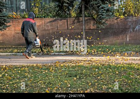 Trockene Blätter mit einer Windmühle reinigen. Ein kommunaler Arbeiter säubert den Stadtpark. Stadtparks für den Winter vorbereiten. Stockfoto