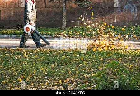 Trockene Blätter mit einer Windmühle reinigen. Ein kommunaler Arbeiter säubert den Stadtpark. Stadtparks für den Winter vorbereiten. Stockfoto