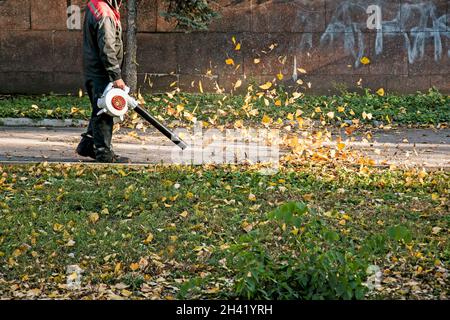 Trockene Blätter mit einer Windmühle reinigen. Ein kommunaler Arbeiter säubert den Stadtpark. Stadtparks für den Winter vorbereiten. Stockfoto